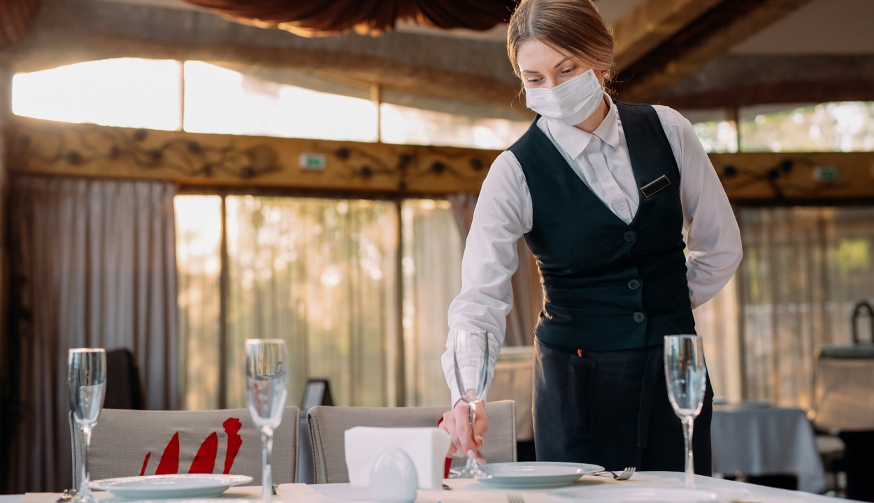 A waiter in a medical protective mask serves the table in the restaurant