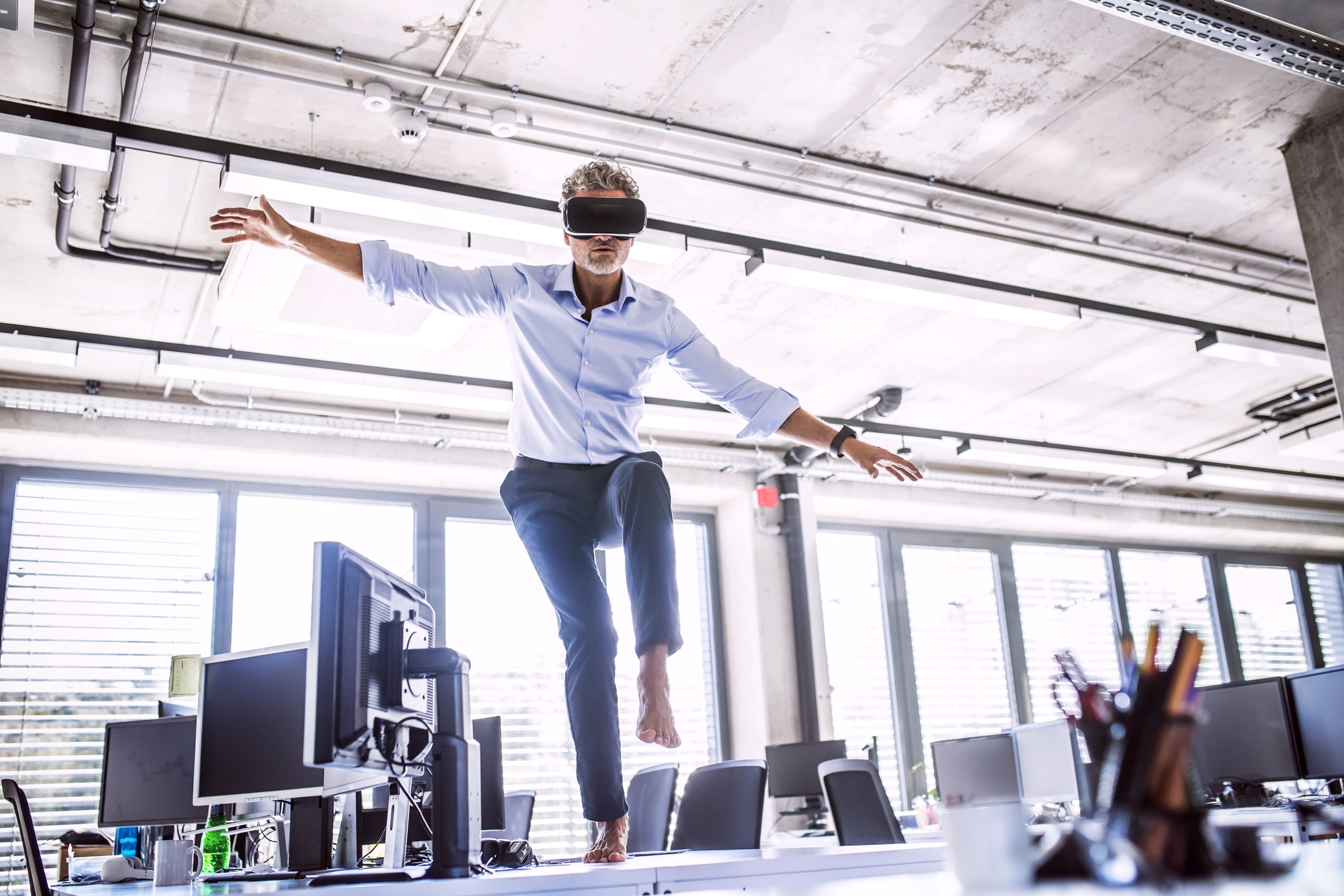 Barefoot mature businessman on desk in office wearing VR glasses