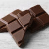 Black chocolate pieces on color wooden background