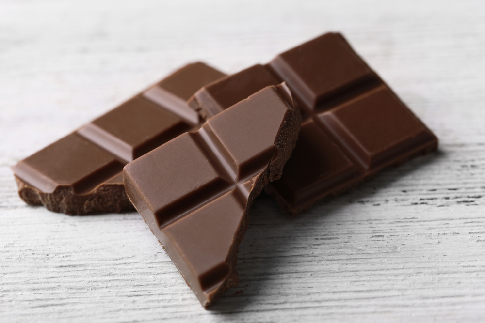 Black chocolate pieces on color wooden background
