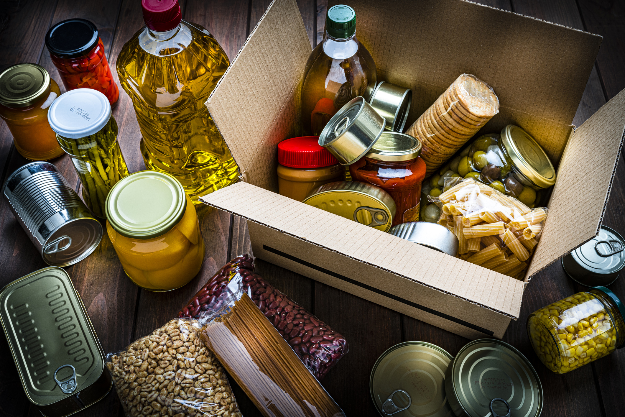 Cardboard box filled with non perishable foods on wooden table. High angle view.